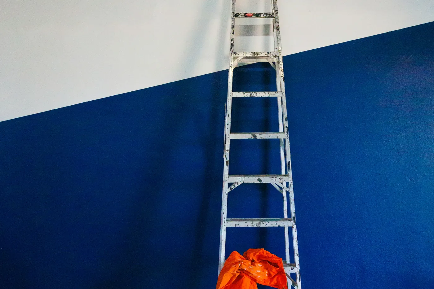 Leiter lehnt an einer halb blau, halb weiss gestrichenen Wand