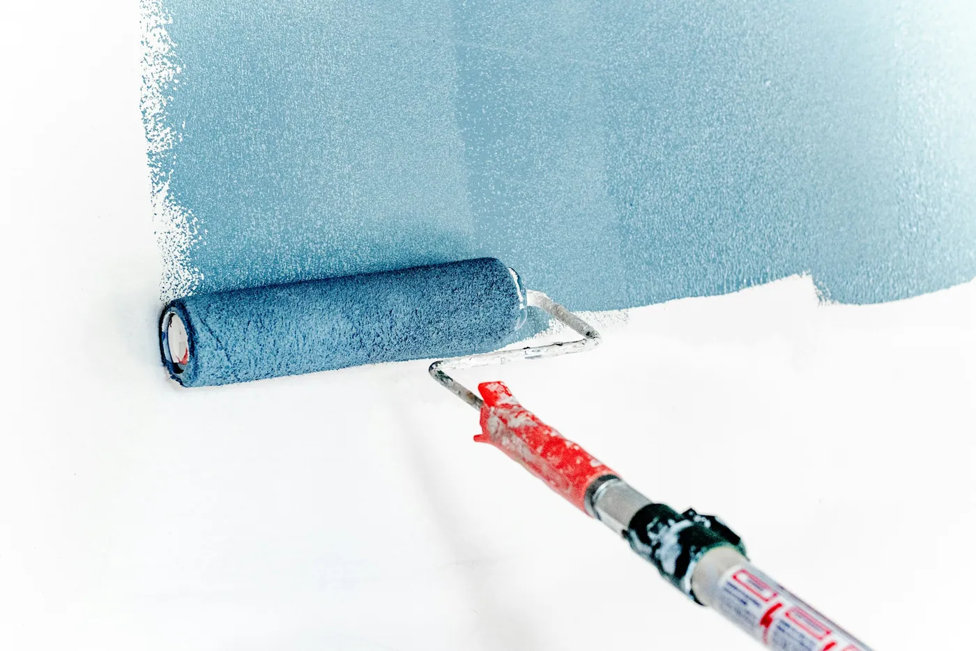 Farbroller zieht blaue Farbe über eine weisse Wand