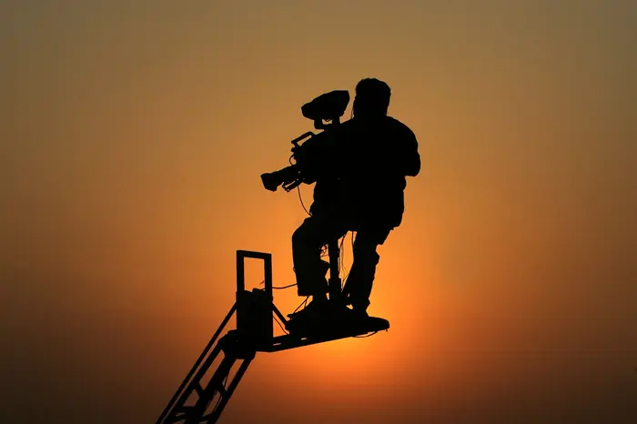 Kameramann auf einem Kamerakran als Silhouette vor Abendrot